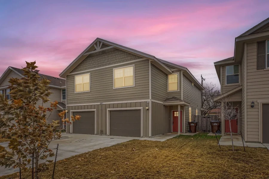 Townhouse exterior with two garages, lit windows and lawn